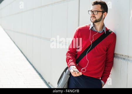 Young businessman using smart phone, wearing ear phones Stock Photo