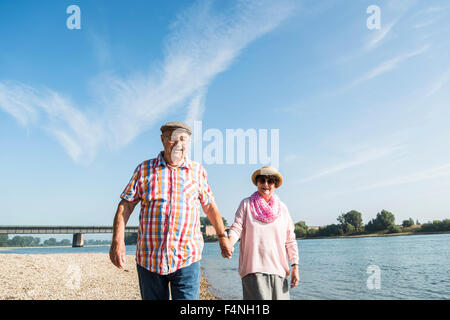 Germany, Ludwigshafen, happy senior couple walking hand in hand at riverside Stock Photo
