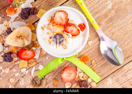 Yogurt with cereals muesli, fresh strawberries, banana and raisins in bowl on wooden background Stock Photo
