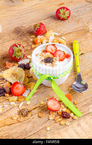 yogurt with cereals muesli, fresh strawberries, banana and raisins in bowl on wooden background Stock Photo