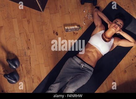 Top view of relaxing young woman lying on fitness mat. Overhead shot of female athlete resting after intense workout with water Stock Photo