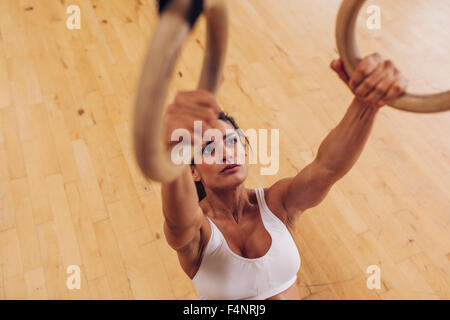 Determined young woman at gym. Muscular female athlete working out using gymnastic rings. Stock Photo