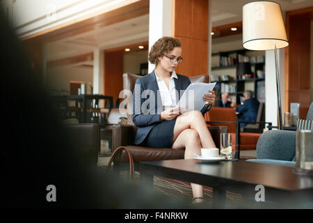 Shot of young business executive sitting at coffee shop reading documents. Caucasian business woman going through some papers. Stock Photo