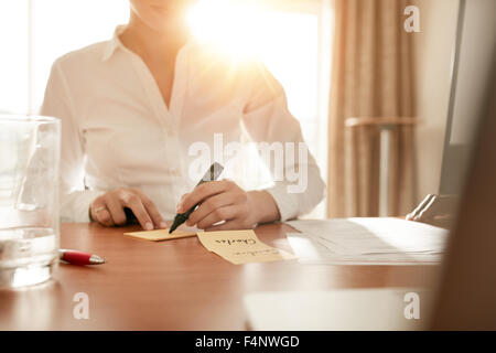 Cropped shot of woman writing some names on sticky notes while sitting in conference room.