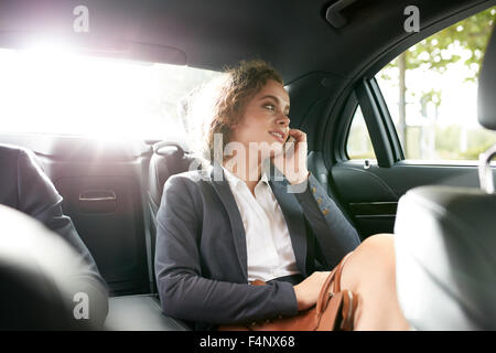 Shot of happy young businesswoman traveling to work in the luxury car on the back seat and talking by phone. Stock Photo