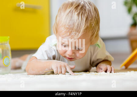 Little child laying on very messy kitchen floor, covered in white baking flour Stock Photo