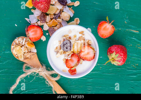 Yogurt with cereals muesli, fresh strawberries, banana and raisins in bowl on wooden background Stock Photo
