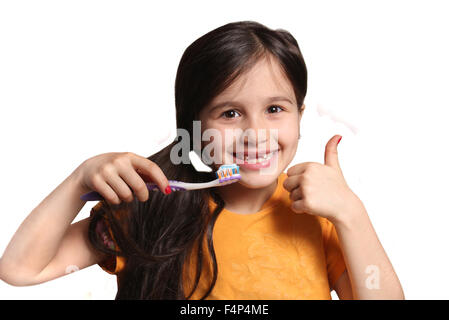 Little seven year old girl shows big smile showing missing top front teeth and holding a toothbrush with toothpaste and thumbs u Stock Photo