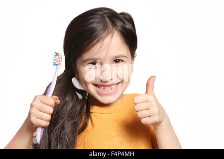 Little seven year old girl shows big smile showing missing top front teeth and holding a toothbrush on a white background Stock Photo
