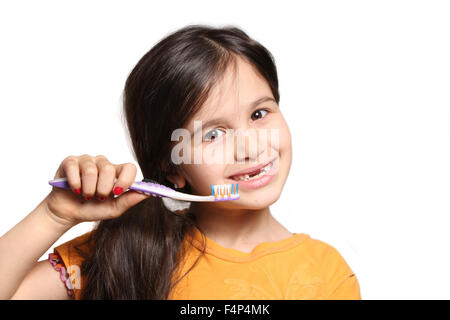 Little seven year old girl shows big smile showing missing top front teeth and holding a toothbrush on a white background Stock Photo