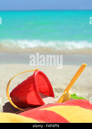 Beach toys and towel in red and yellow in  sand on a tropical Caribbean beach with blue ocean in the background Stock Photo