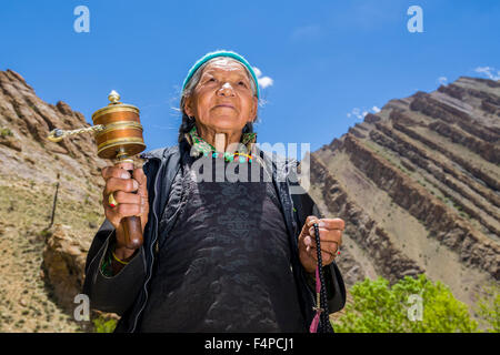 An old ladakhi woman is turning a prayer wheel in a small valley above Hemis Gompa Stock Photo