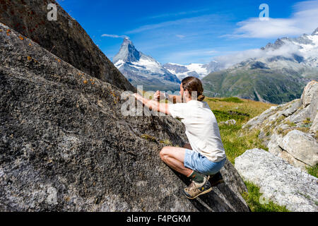 Climber uses his smartwatch on a boulder under the famous Matterhorn peak. July, 2015. Matterhorn, Switzerland. Stock Photo