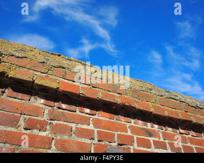 Bottom view on a fragment of red brick fence against a bright blue sky with clouds on the diagonal of the frame. Stock Photo