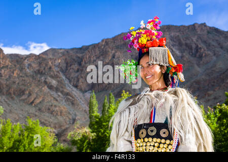 A woman of the Brokpa tribe, an arien race, in her traditional dress with a flower arrangement carried on the head Stock Photo