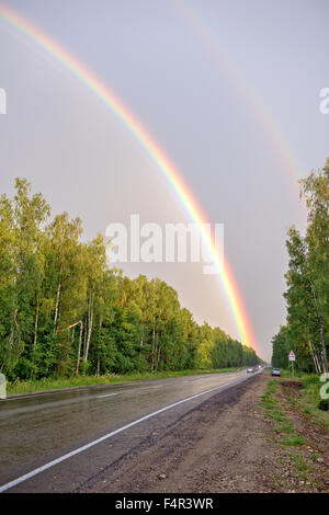 Double rainbow in sky over road and forest Stock Photo