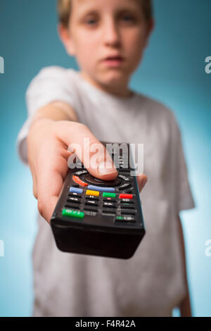 A bored boy changing channels using a TV remote control Stock Photo