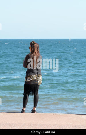 Young woman standing on steps looking out at Torbay from Oddicombe beach on hot September day in Torquay, Devon, England Stock Photo
