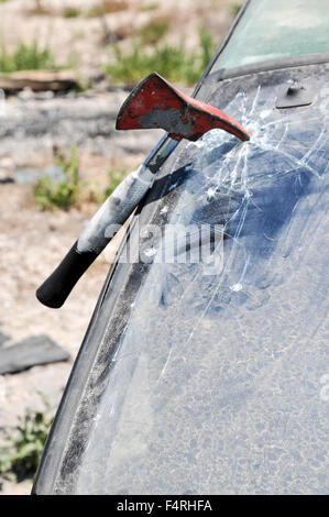 Firefighter uses an axe to break the front windshield of a car to rescue the trapped driver and passengers Stock Photo