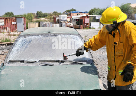 Firefighter uses an axe to break the front windshield of a car to rescue the trapped driver and passengers Stock Photo