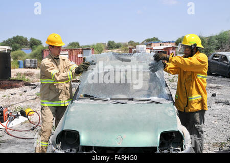 Firefighter uses an axe to break the front windshield of a car to rescue the trapped driver and passengers Stock Photo