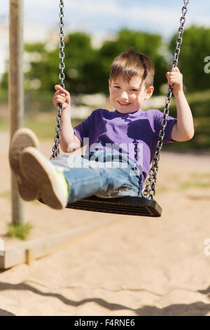 happy little boy swinging on swing at playground Stock Photo