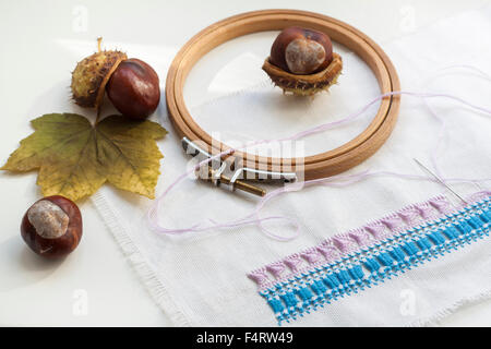 Mature chestnuts, autumn leaves and needlework on white background Stock Photo