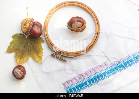 Mature chestnuts, autumn leaves and needlework on white background Stock Photo