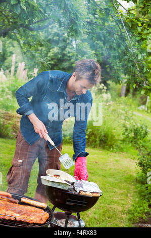 Sweden, Ostergotland, Vikbolandet, Mid-adult man having barbecue in backyard Stock Photo
