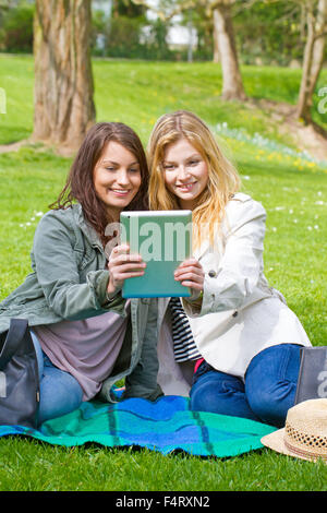Two happy girls with tablet sitting in a park Stock Photo