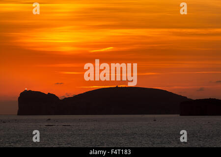 Dramatic glowing orange sunset over the lighthouse of Capo Caccia on the north west coast of Sardinia Stock Photo