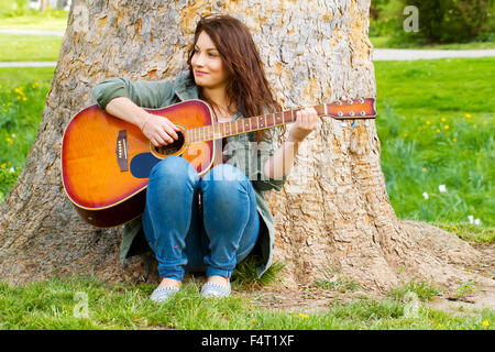 Girl with guitar sitting on a tree Stock Photo