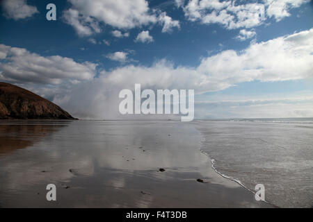 Passing clouds reflected in tide water on Newgale Beach, Pembrokeshire on a spring day with blue sky, cloud and incoming sea Stock Photo