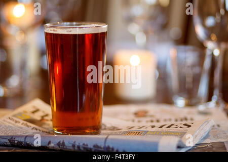 A pint of beer on a pub table with newspapers Stock Photo