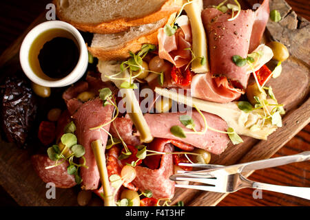 A Mediterranean meat board with hams, bread, olives, artichoke, sun-dried tomato and pickled onions Stock Photo