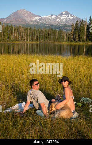 USA, Oregon, Lane County, Willamette, National Forest, Scott Lake, couple with dog tanning at lake Stock Photo