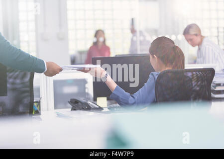Businessman handing paperwork to businesswoman at desk Stock Photo