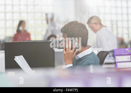 Businessman with paperwork talking on cell phone in office Stock Photo