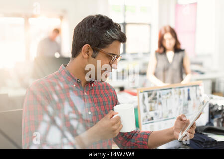 Fashion designer using digital tablet and drinking coffee in office Stock Photo