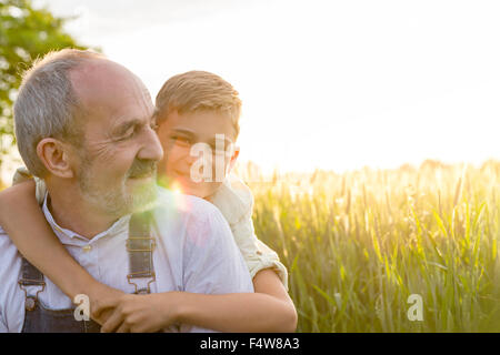 Portrait affectionate grandson hugging grandfather in rural wheat field Stock Photo