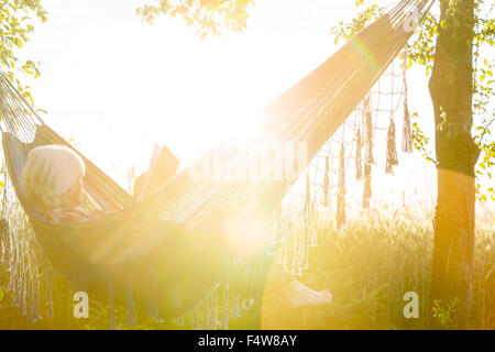 Serene woman reading book in sunny hammock Stock Photo