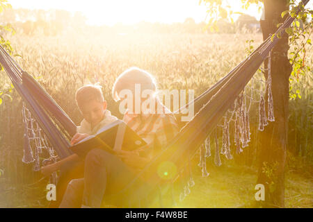 Grandmother and grandson reading book in sunny rural hammock Stock Photo