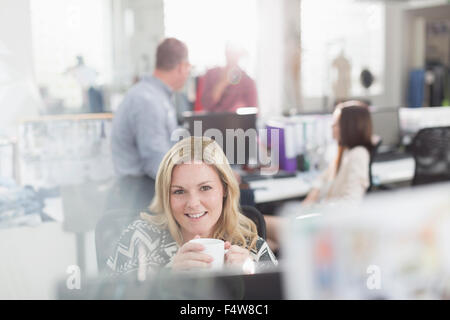 Portrait smiling fashion designer drinking coffee at computer in office Stock Photo