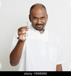 Portrait of Indian man holding new house key, real estate property agent concept, standing on plain background with shadow. Stock Photo