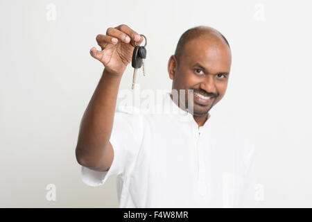 Mature Asian Indian estate agent or salesman showing a key, India male business man, standing on plain background with shadow. Stock Photo