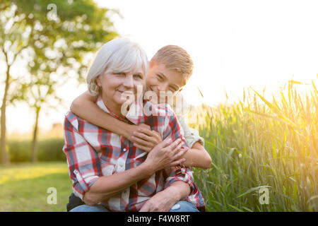 Portrait smiling grandmother and grandson hugging near sunny rural wheat field Stock Photo
