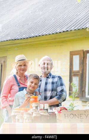 Portrait proud grandparents and grandson selling honey at farmer’s market stall Stock Photo