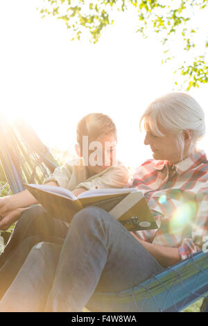 Grandmother reading to grandson in sunny hammock Stock Photo