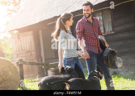 Couple with saddle and dogs holding hands outside rural barn Stock Photo