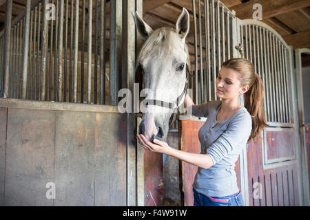 Woman feeding horse at stable stall Stock Photo